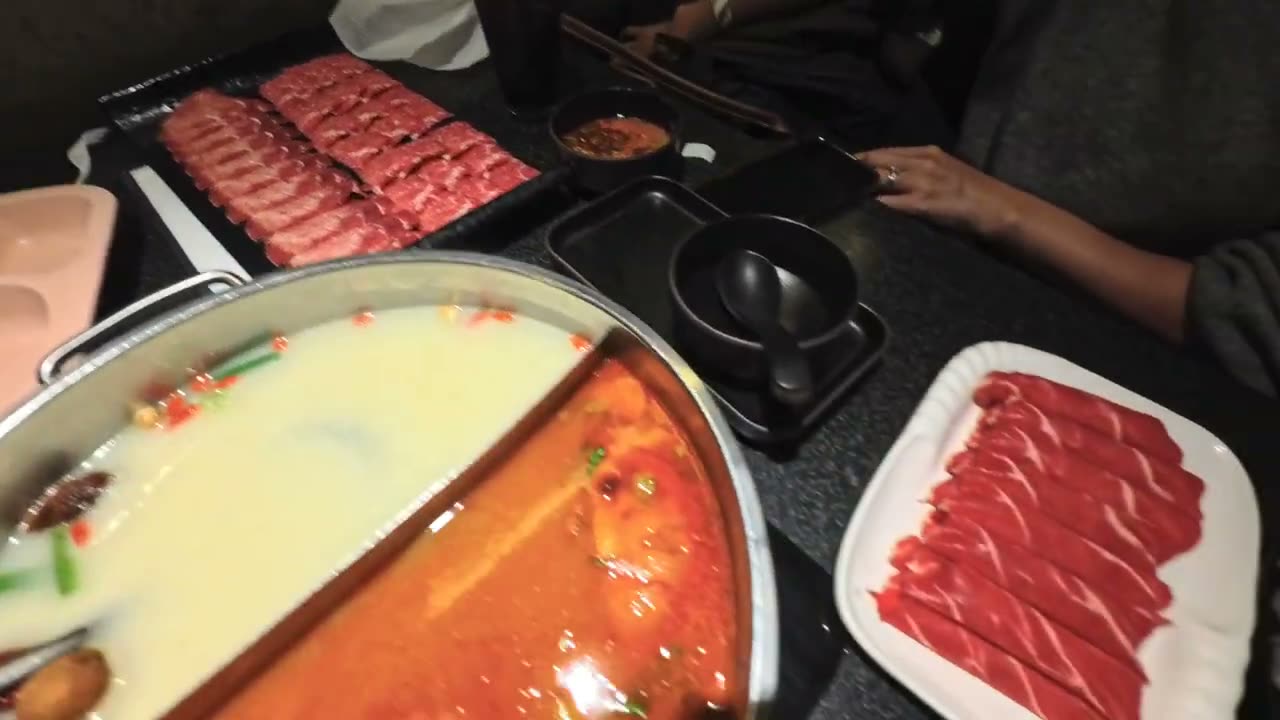 A two-sided pot of bone marrow broth and tomato broth with plates of beef at Happy Lamb in Edison