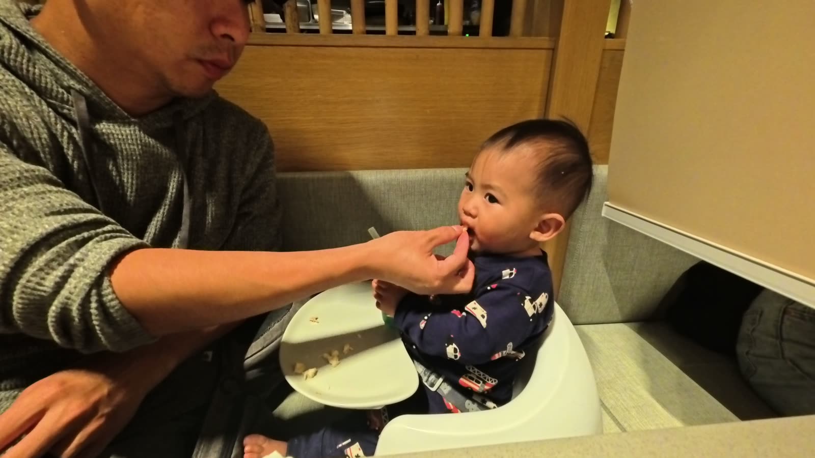 Michael feeding Archie in a booster seat at the hotpot table