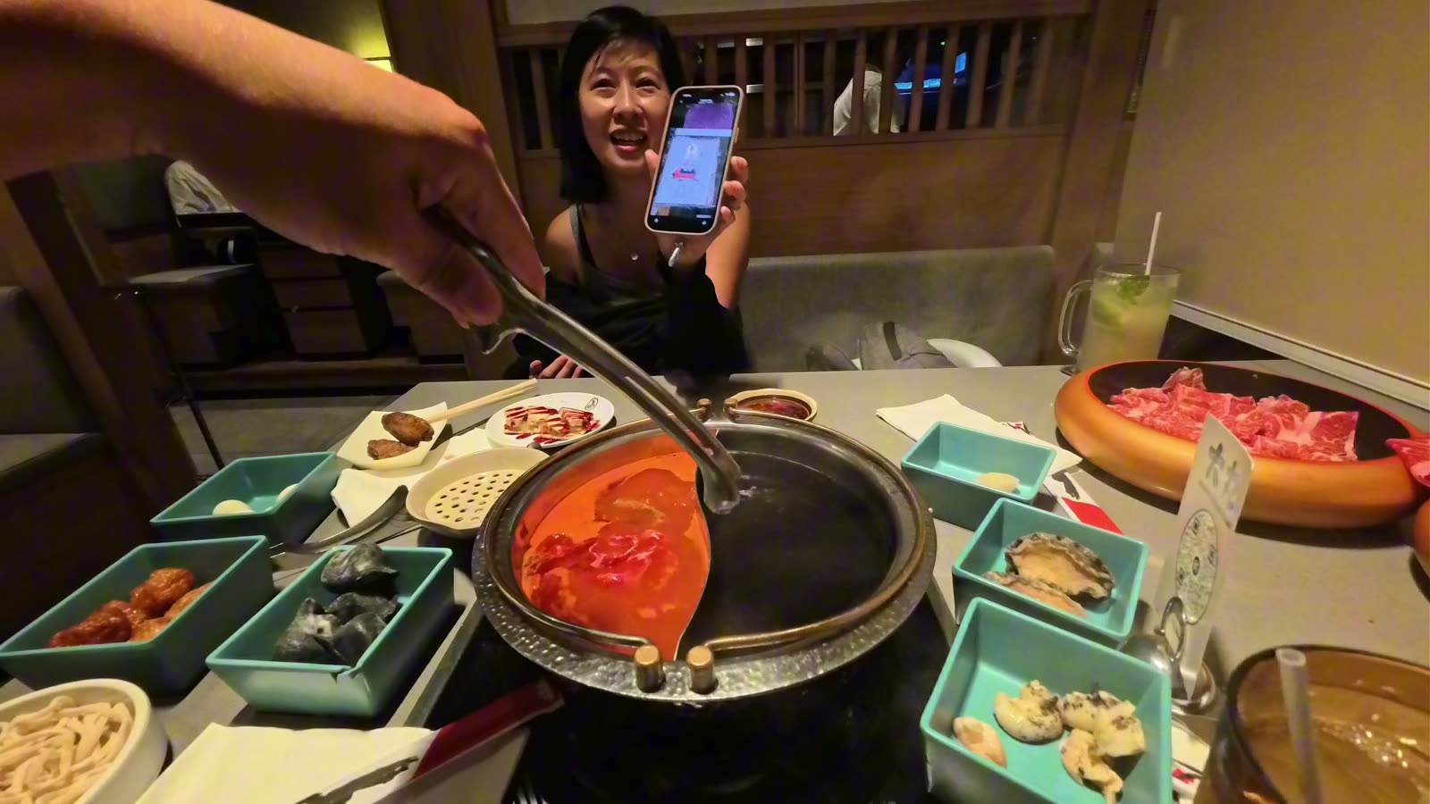 Hotpot with tomato broth on one side and sukiyaki on the other, surrounded by plates of wagyu, abalone, squid ink dumplings and wings