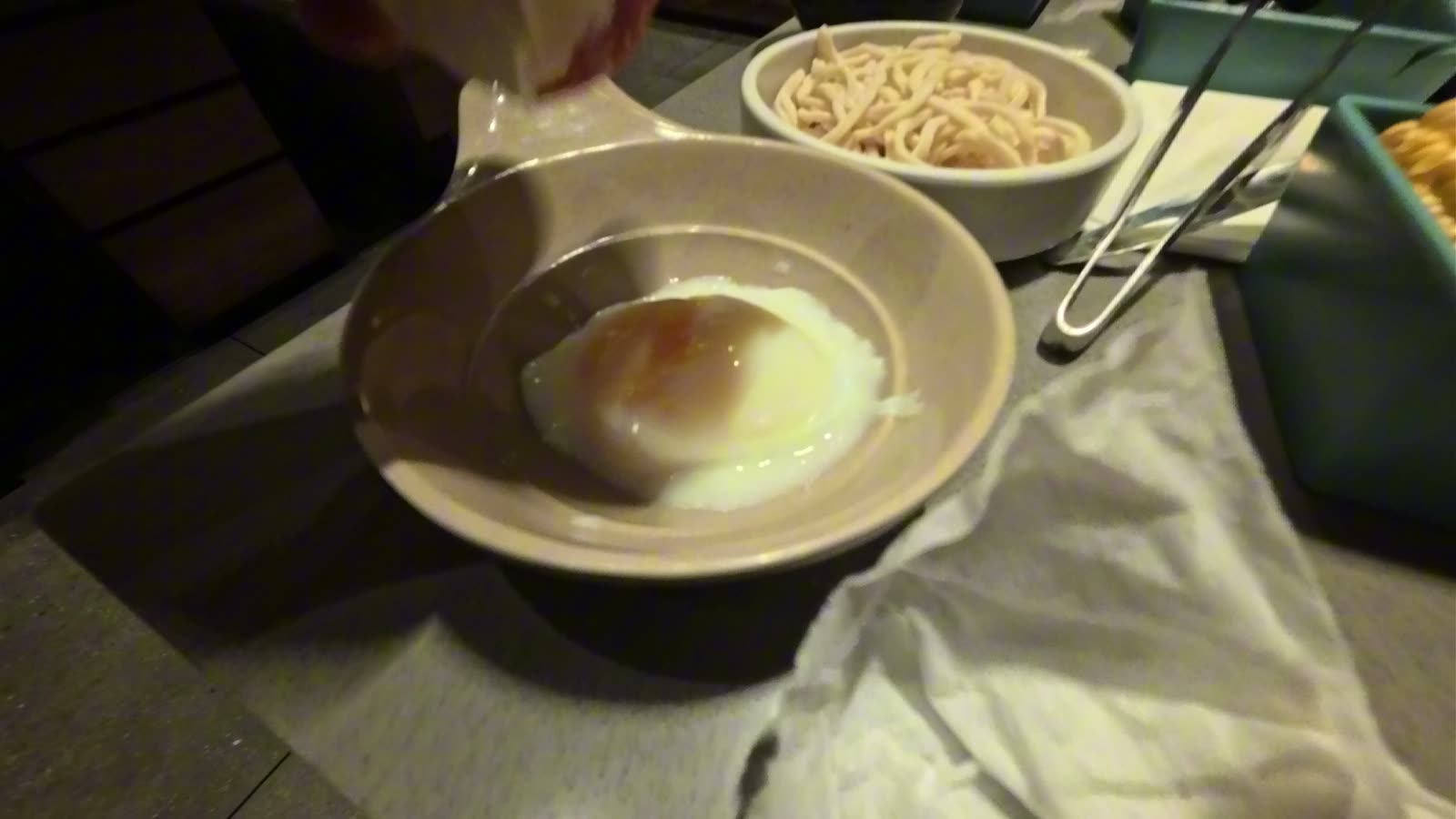 A soft onsen egg in a small bowl next to a bowl of noodles