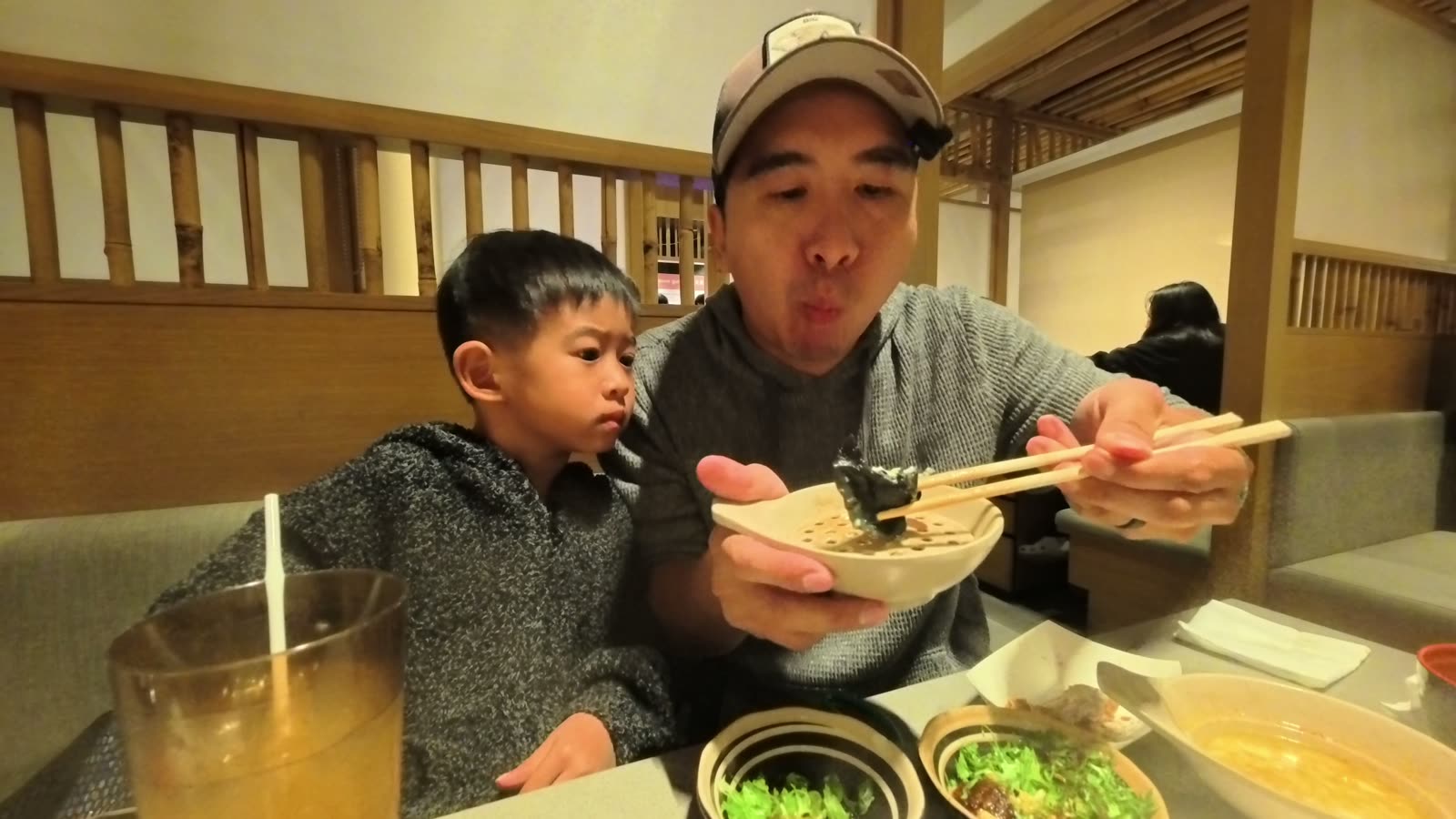 Michael holding up a black squid ink dumpling with chopsticks while Spencer watches