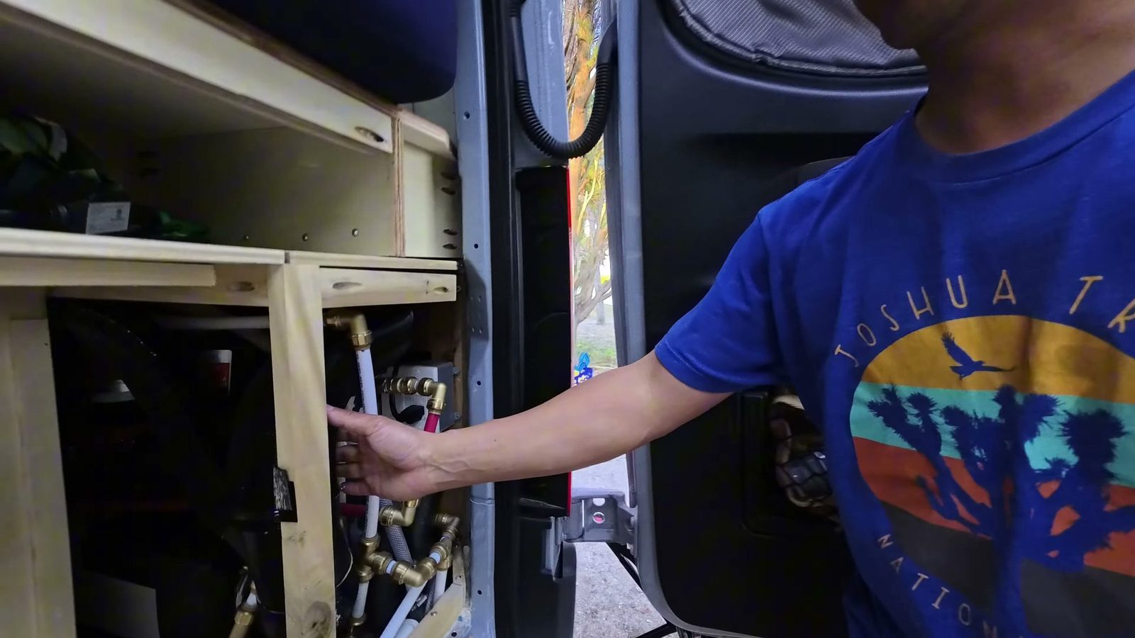 Brass push-to-connect fittings and white PEX lines in the water compartment of our van