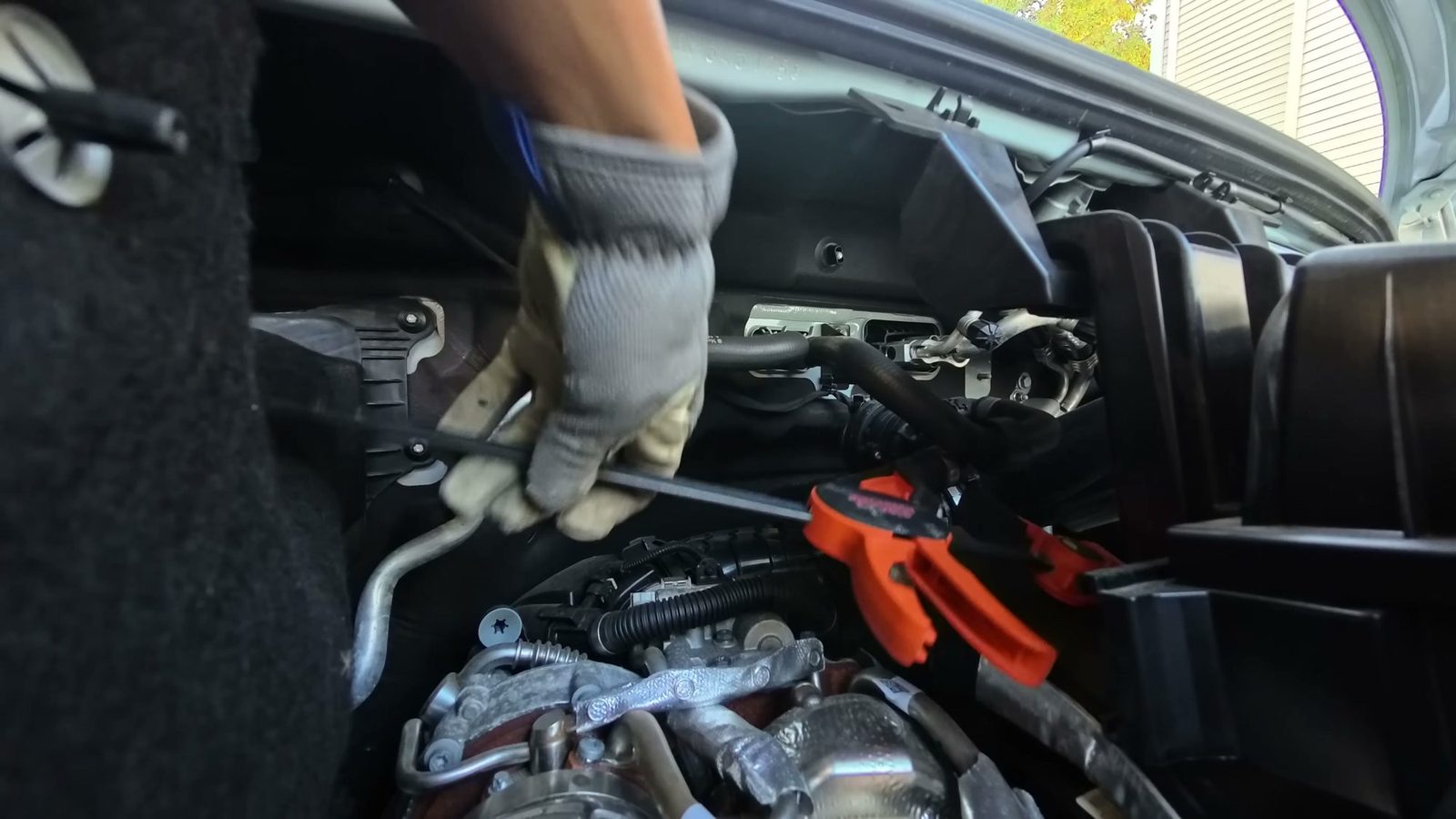 Gloved hands and an orange clamp on the engine coolant hose before cutting