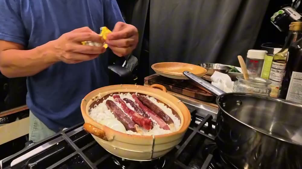 A clay pot of rice topped with whole Chinese sausages on the van stove, with Michael peeling a salted duck egg above it