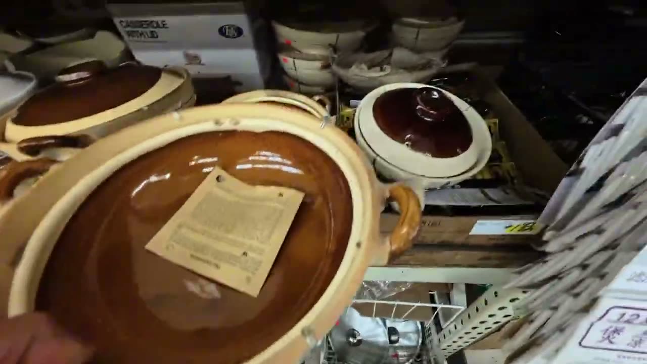 Holding up a brown glazed clay pot with a paper label inside it on a supermarket shelf