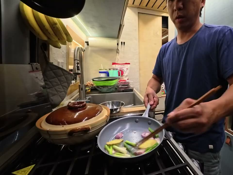 Shallots, scallion whites and ginger cooking in a small pan next to the clay pot on the van stove