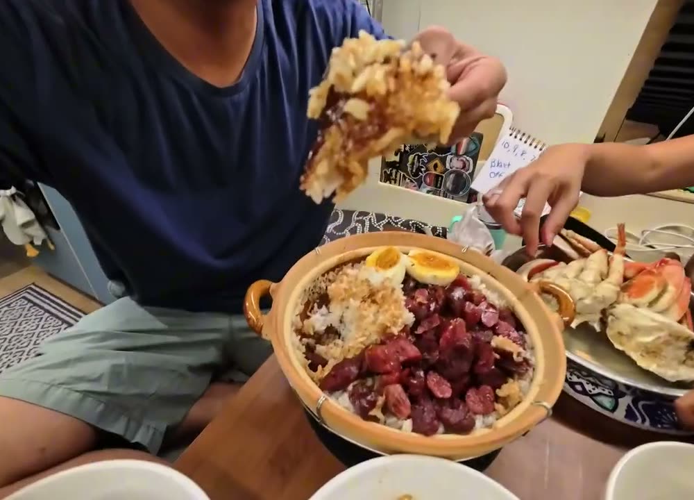 Michael holding up a big piece of golden crispy rice crust over the clay pot at the dinner table in the van