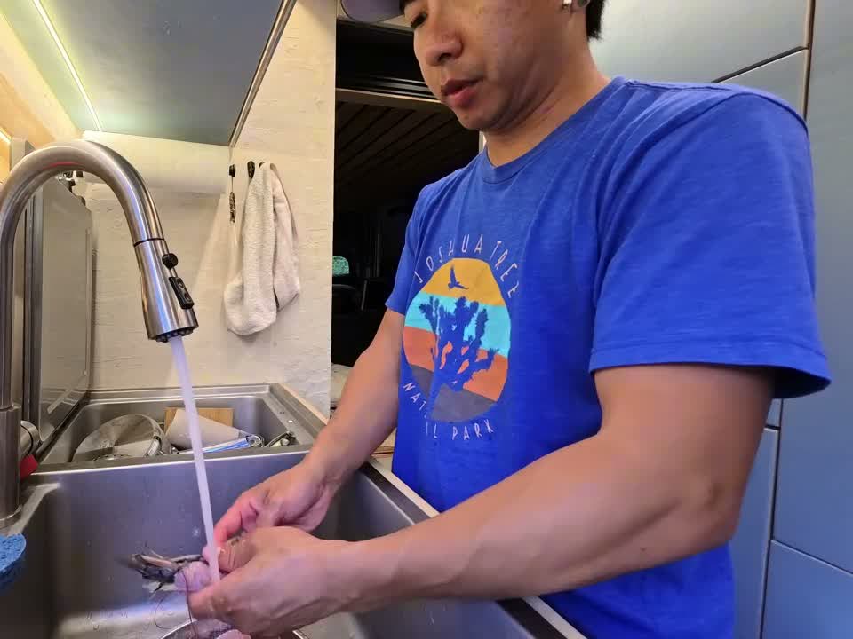 Michael rinsing shrimp under the faucet at the stainless steel sink inside the van