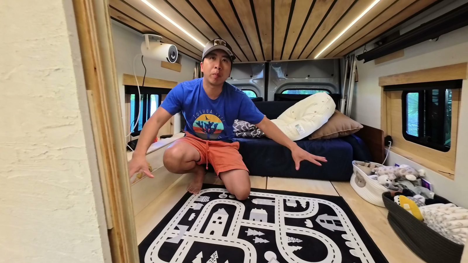 Michael kneeling on the raised play platform in the back of our van, with a road-map play rug and baskets of toys