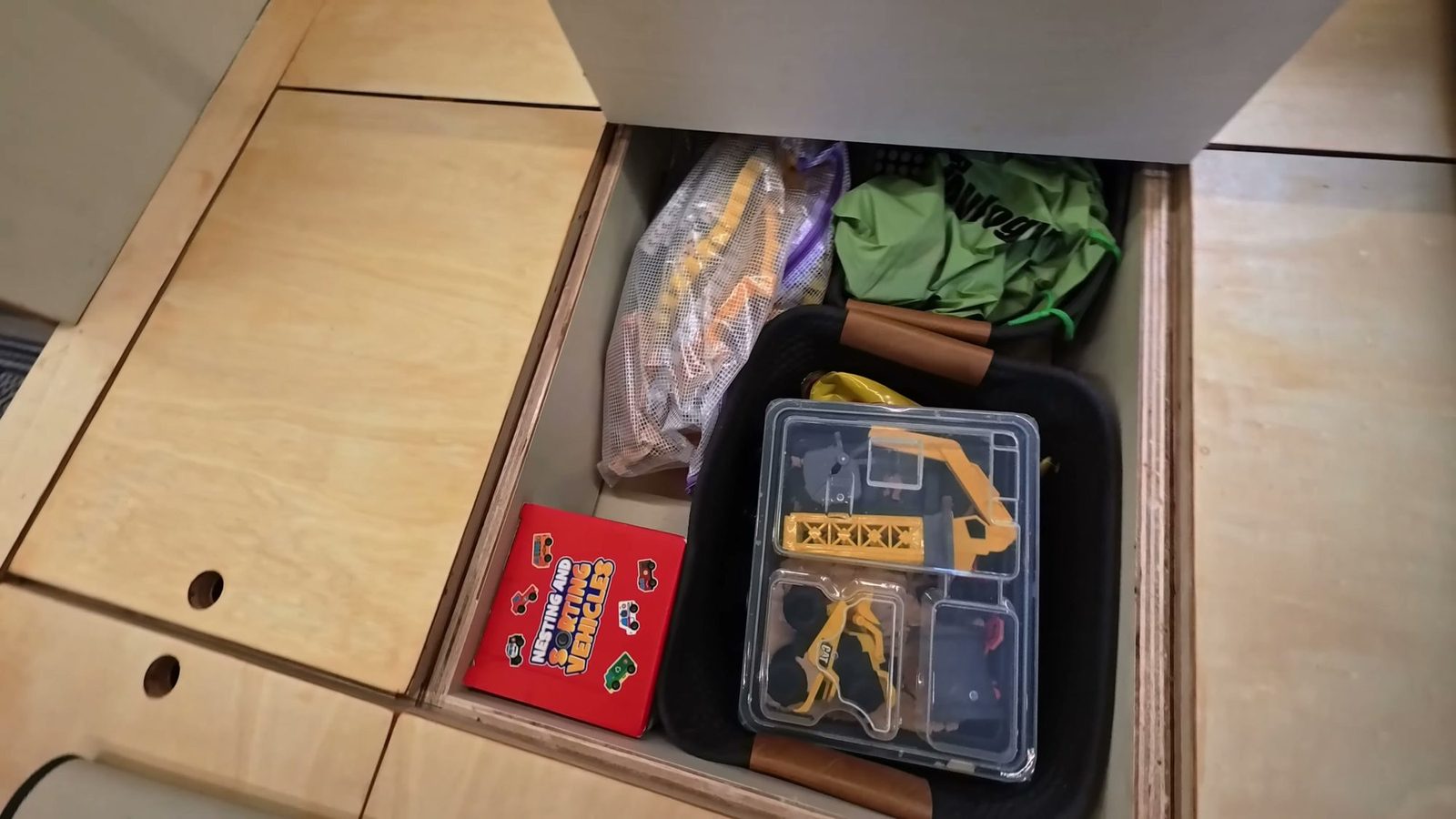 The play platform with a lid lifted, showing toys and gear stored in the cubby underneath