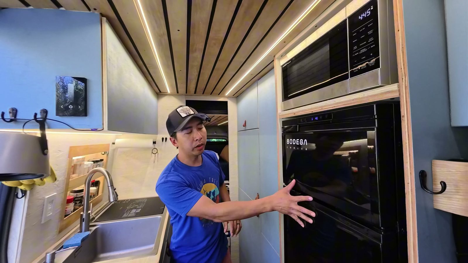 Michael in the hallway kitchen next to the upright fridge and microwave, with the sink on the left