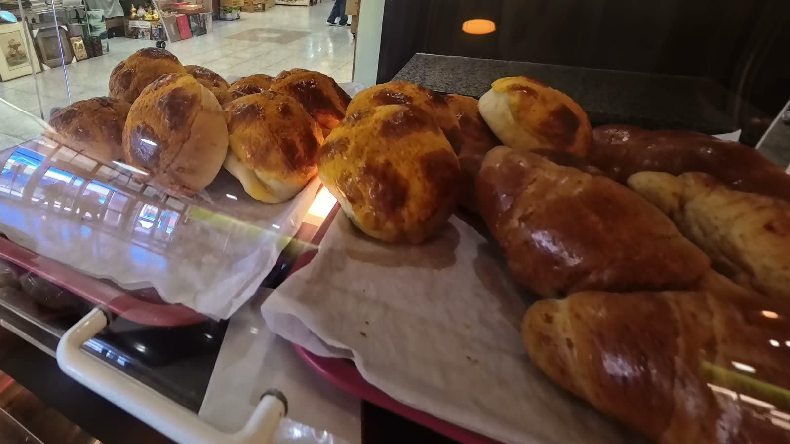 Pineapple buns with a golden cracked top behind a bakery display cover