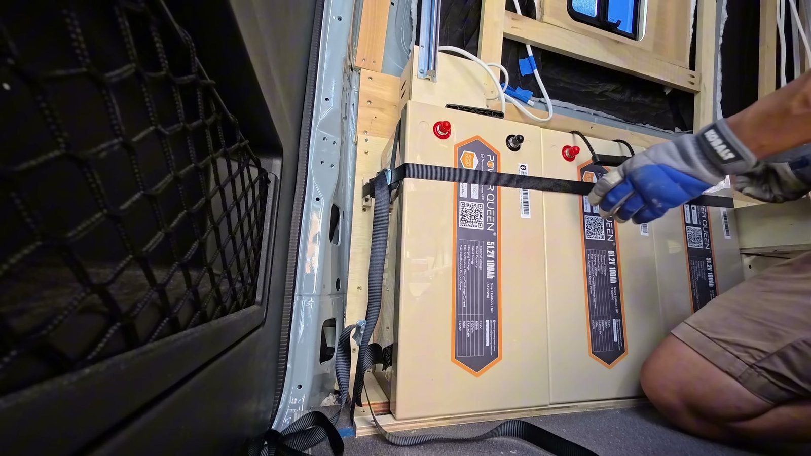 Three Power Queen 51.2V 100Ah batteries standing on their side behind the rear wheel well, being strapped down