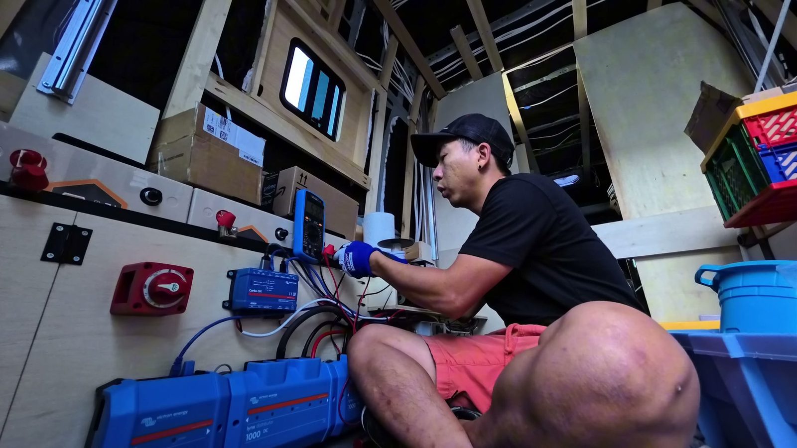 Michael wearing gloves, checking a battery terminal with a multimeter next to the Victron Lynx panel