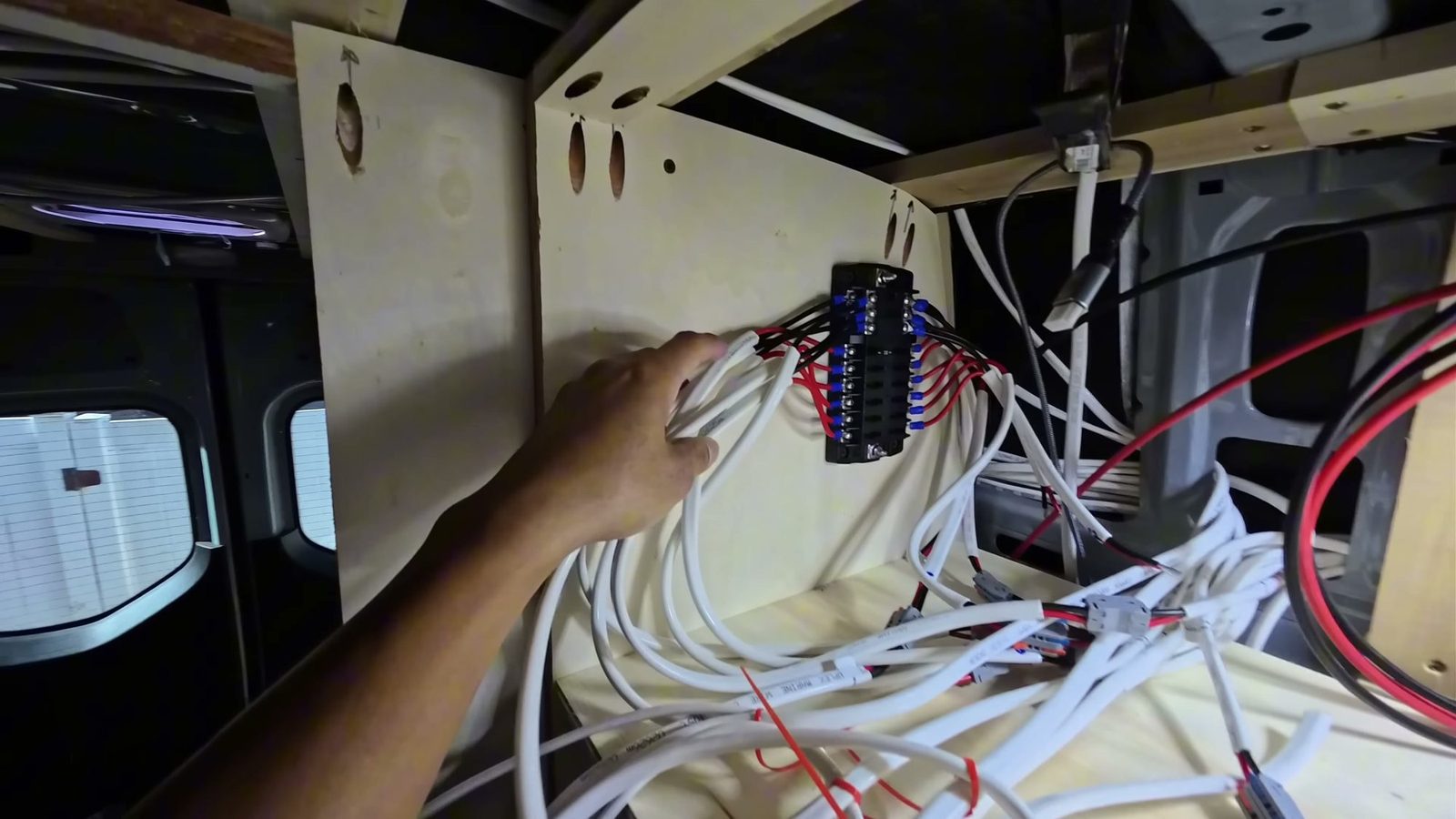A 12V fuse block on the cabinet wall with dozens of labeled white marine wires and pre-crimped pigtails