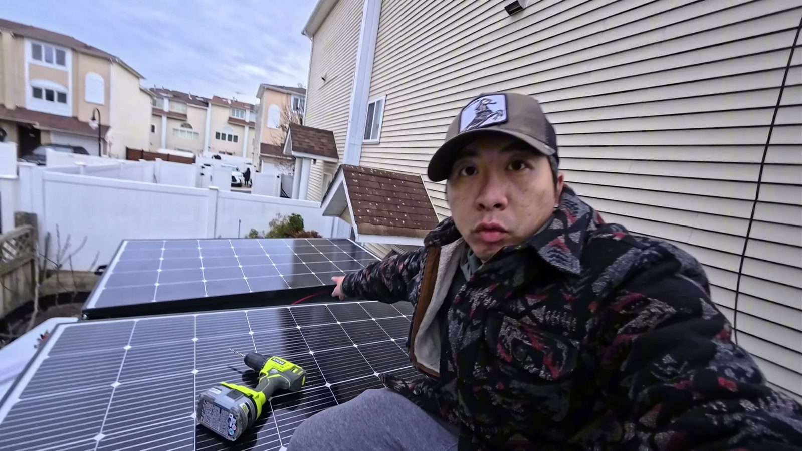 Michael sitting on the van roof next to two of the solar panels, with a drill resting on one of them