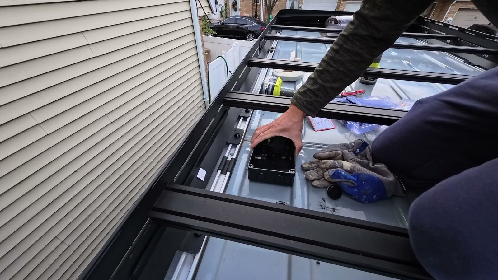 Michael placing a black junction box on the bare van roof between the bars of the roof rack