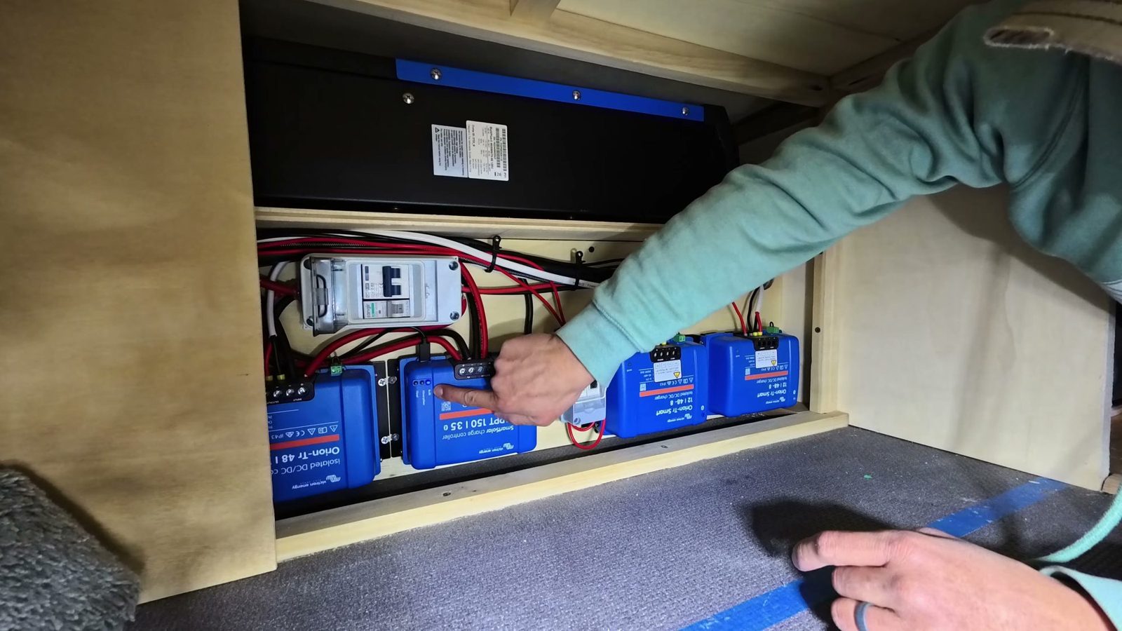Michael pointing at the blue Victron solar charge controller inside the van’s electrical cubby