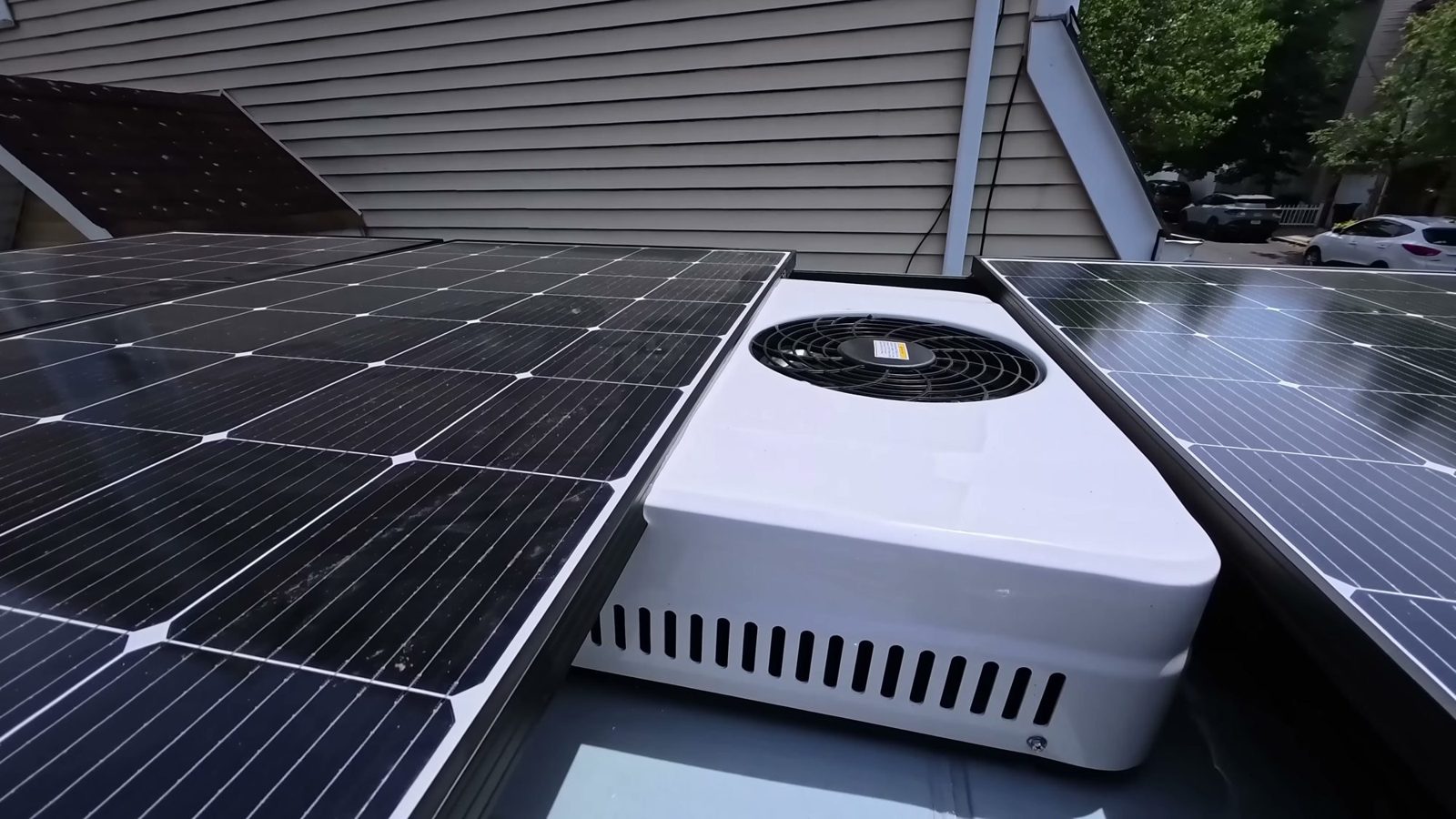 A white rooftop air conditioner sitting in the gap between two solar panels on the van roof