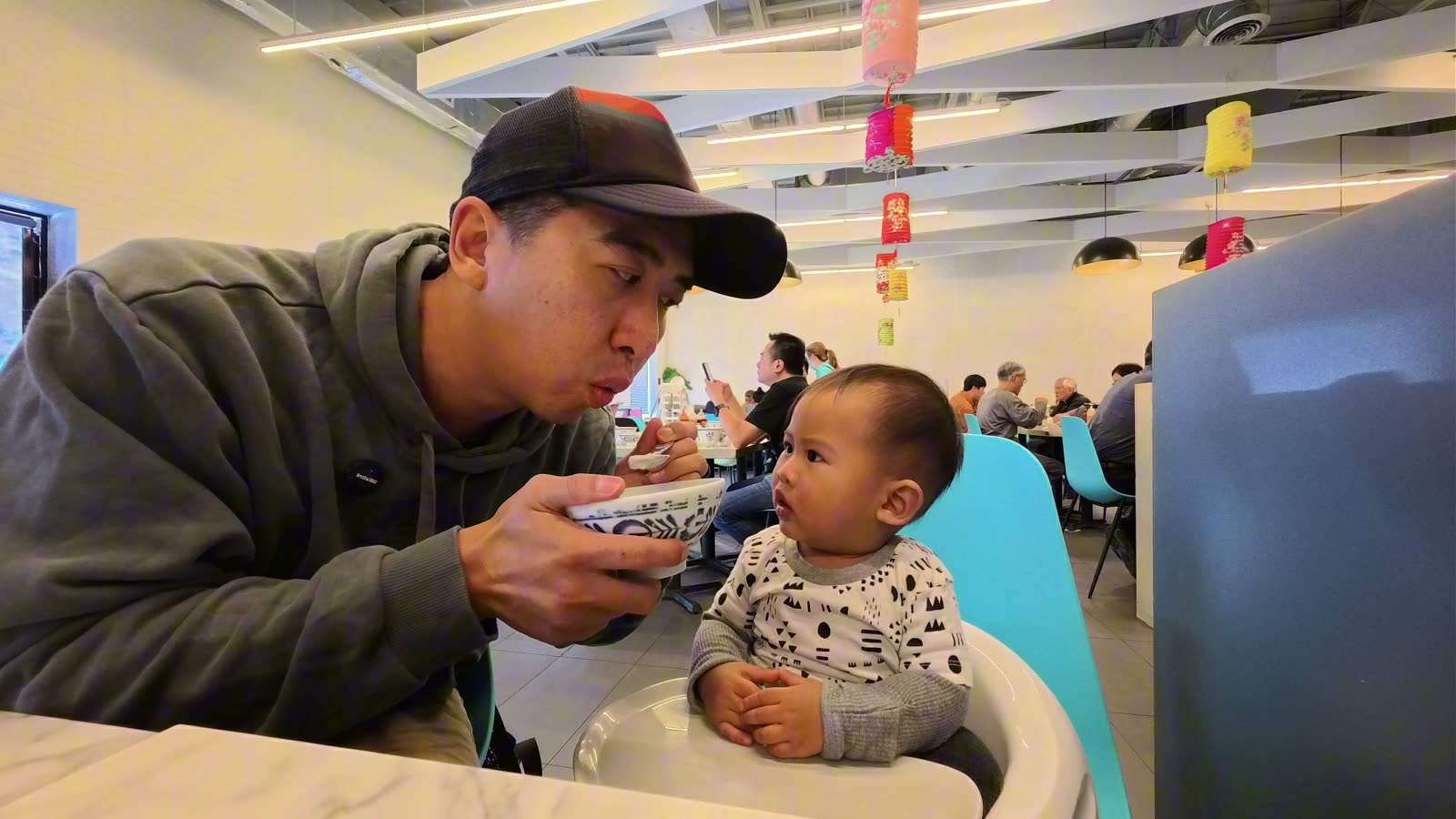 Michael cooling a spoonful of congee for Archie in a high chair at Sam’s Congee Delight