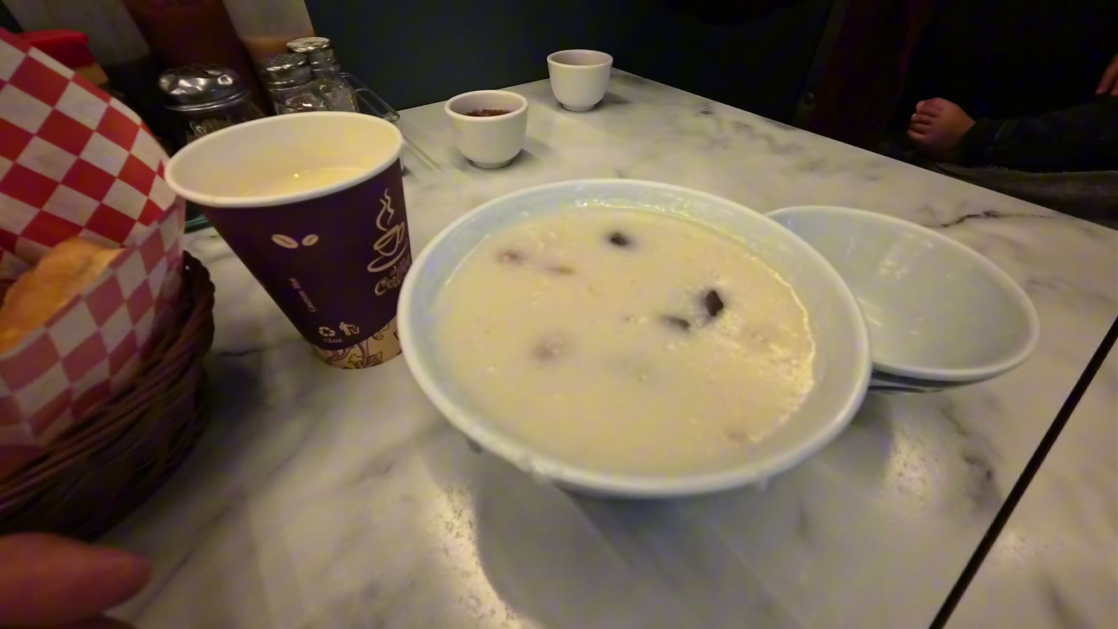 A bowl of congee with pork blood next to a cup of fresh soy drink