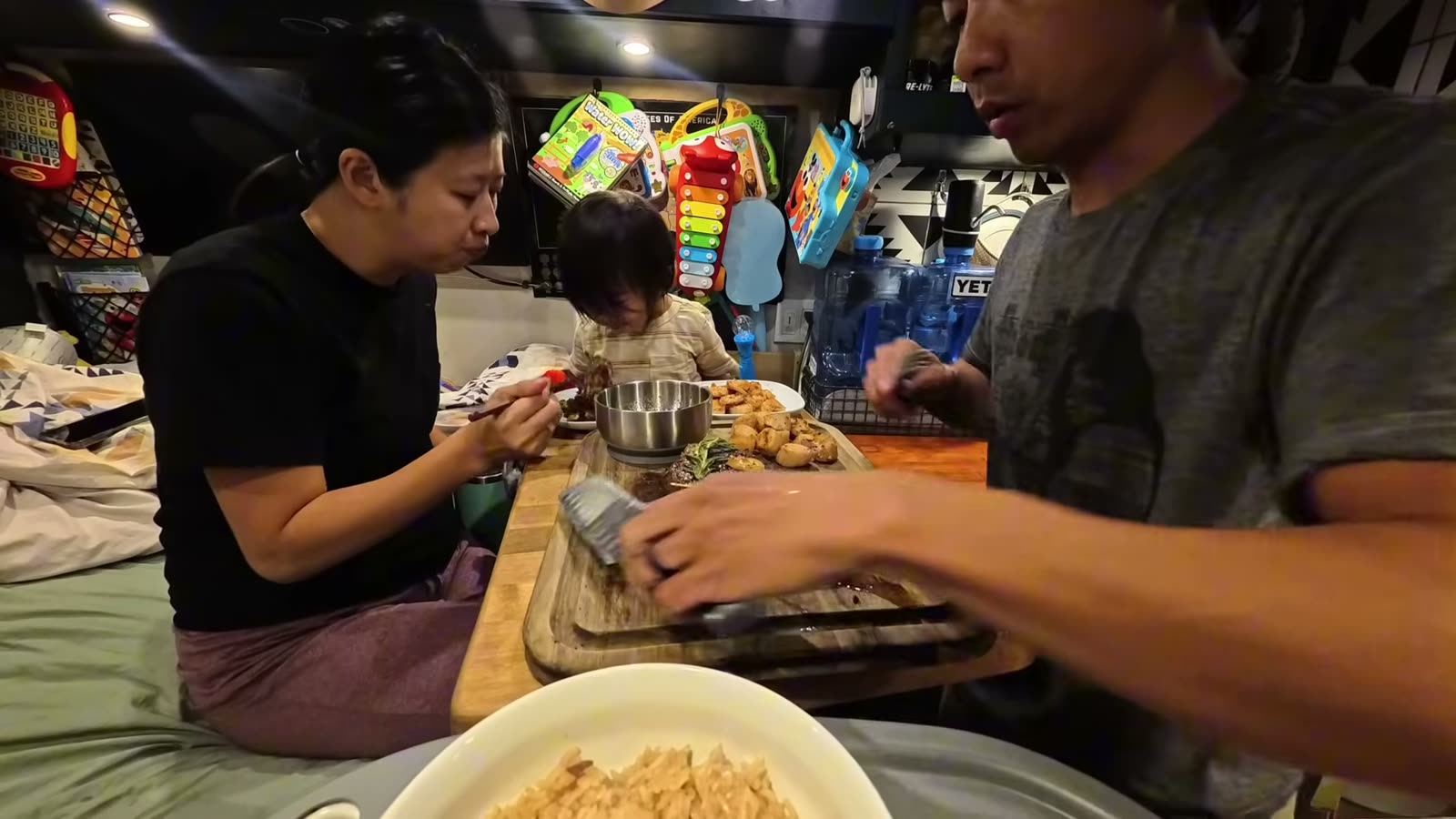 Rina and Spencer eating at the table inside our van at night while Michael serves dinner