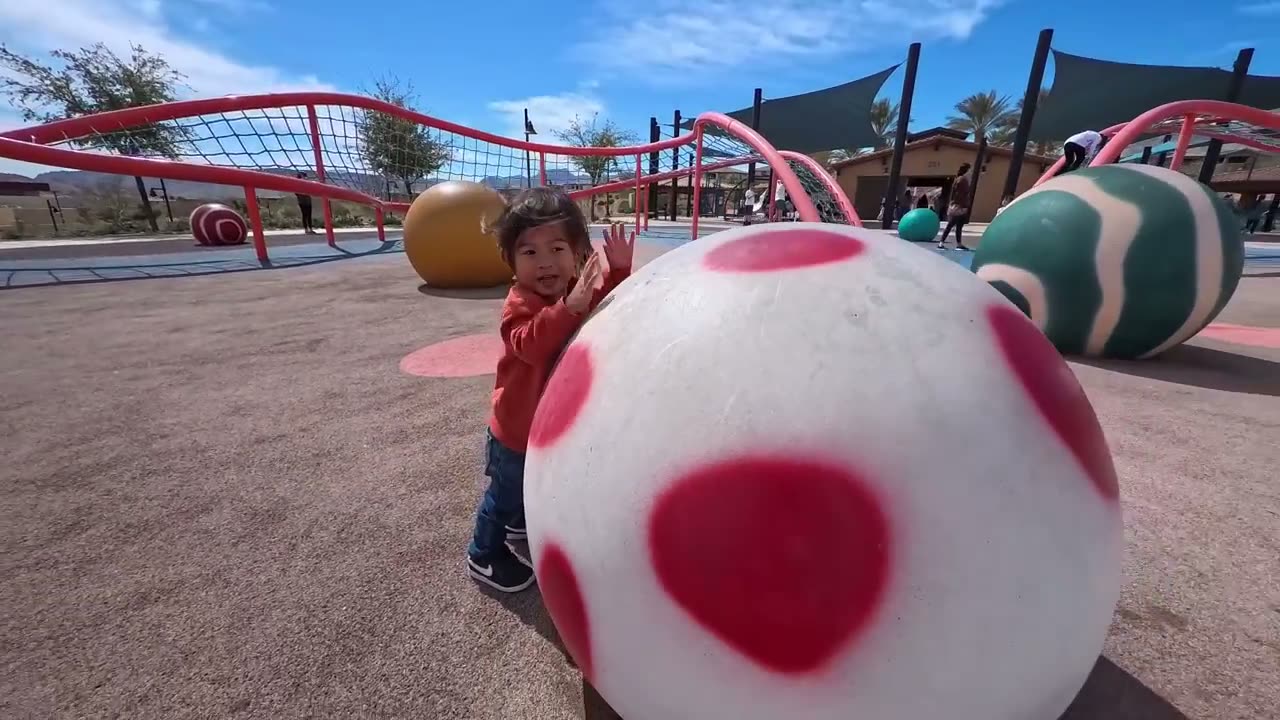 Spencer smiling behind a giant spotted ball at Fox Hill Park playground in Las Vegas