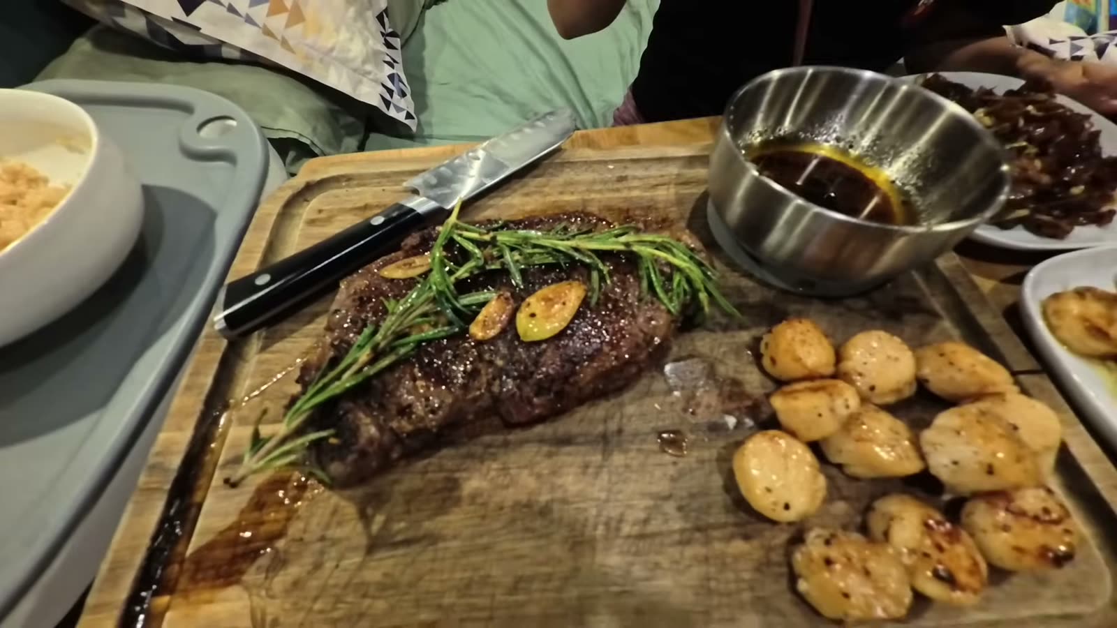 Seared ribeye with rosemary and garlic next to seared scallops on a wooden board inside our van