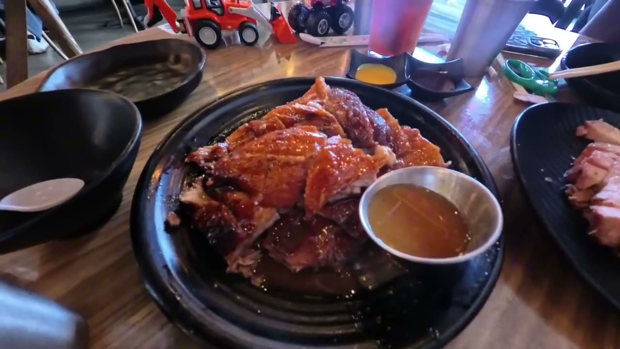 Half a Hong Kong roast duck with crispy skin and a cup of dipping sauce on a black plate at Win Kee in Las Vegas