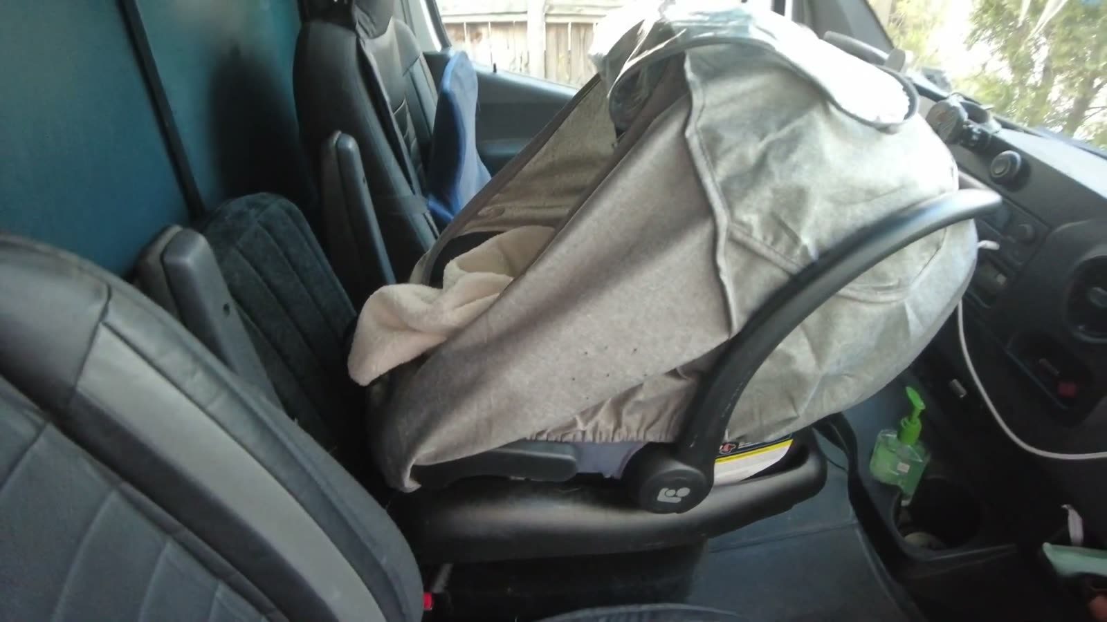 An infant car seat with a grey canopy installed on the middle jump seat between the two front seats of our first van