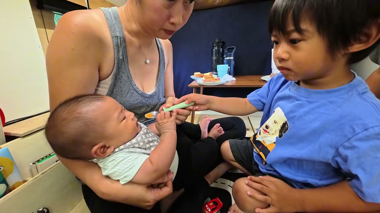 Spencer feeding baby Archie with a small spoon while Rina holds Archie inside the van