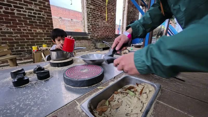 Spencer playing with sand and cooking pots at an outdoor play kitchen at a children’s museum