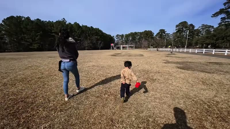 Rina and Spencer walking across a big grassy park next to a playground on a sunny winter day