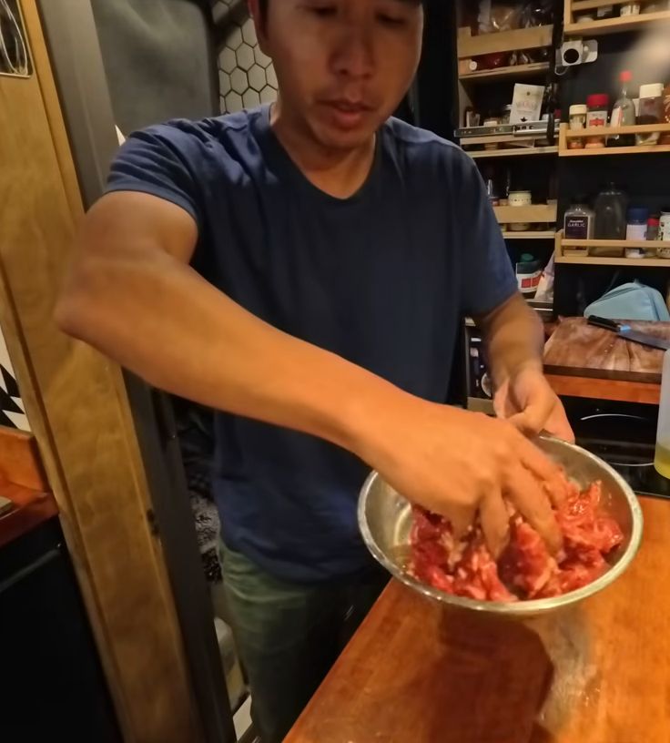 Michael mixing the marinade into thin slices of beef in a metal bowl in the van