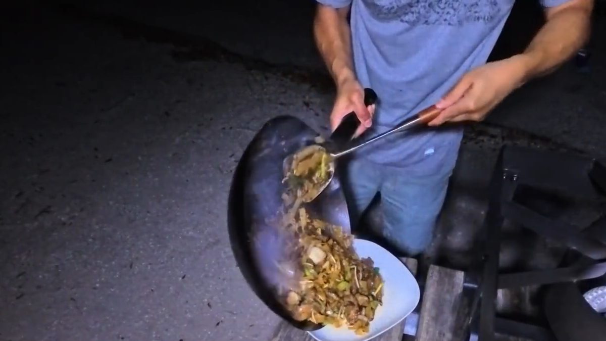 Michael tipping beef chow fun from the wok onto a plate at night at the campground