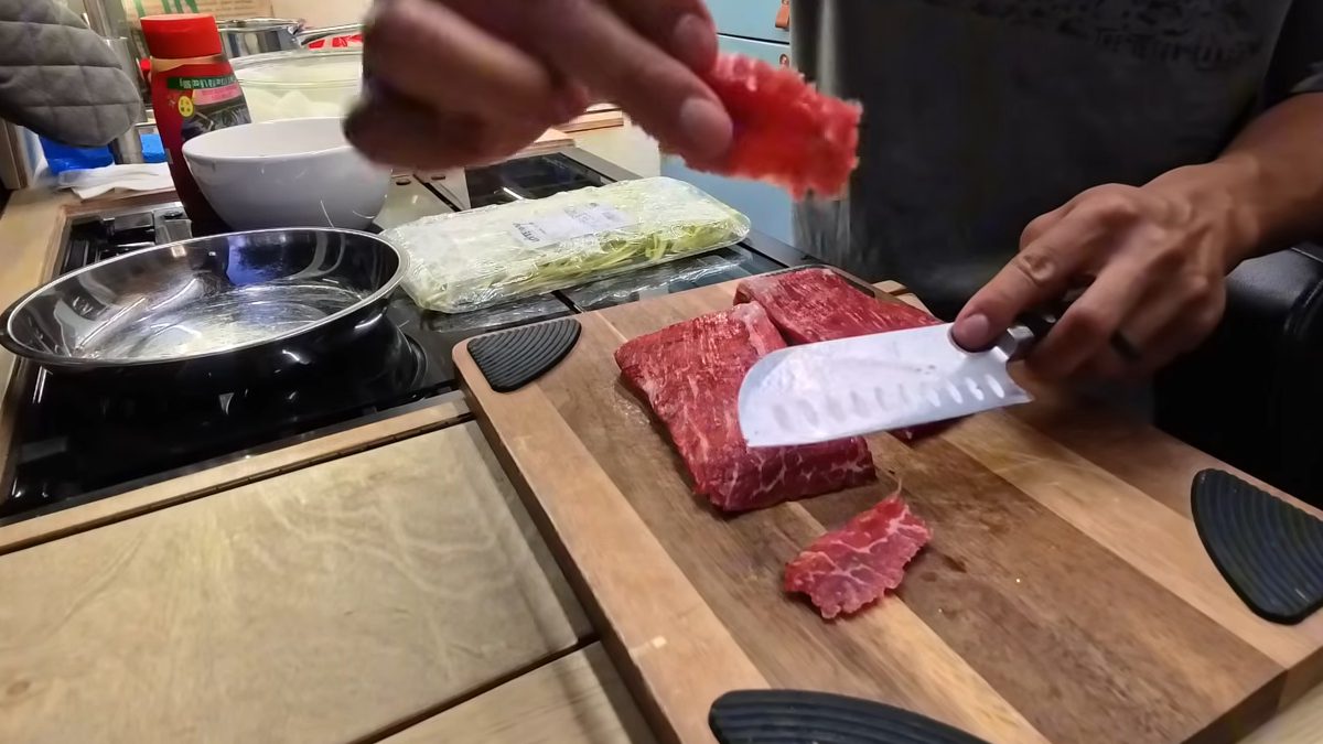 Slicing flank steak against the grain on a cutting board in our van kitchen