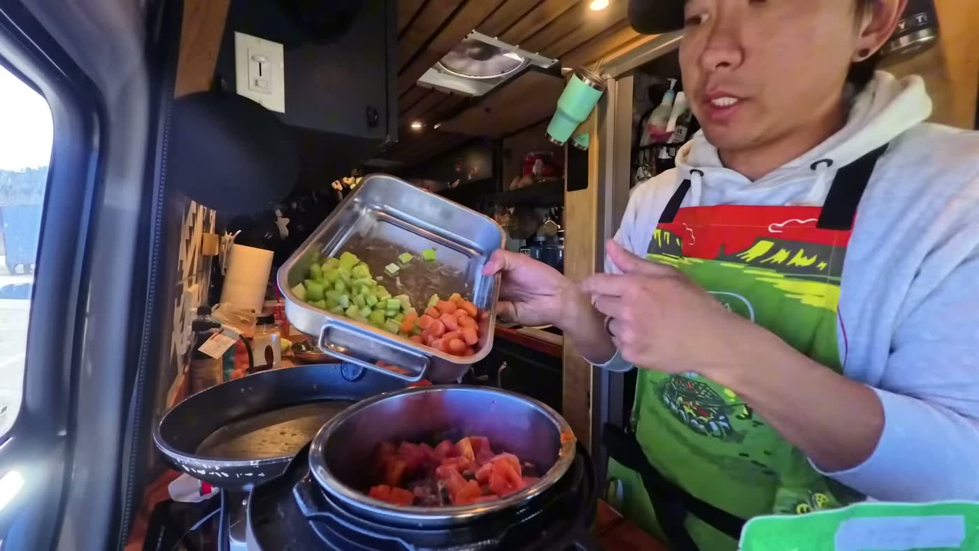 Michael holding a dish of chopped celery, carrot and tomato over the pressure cooker in the van