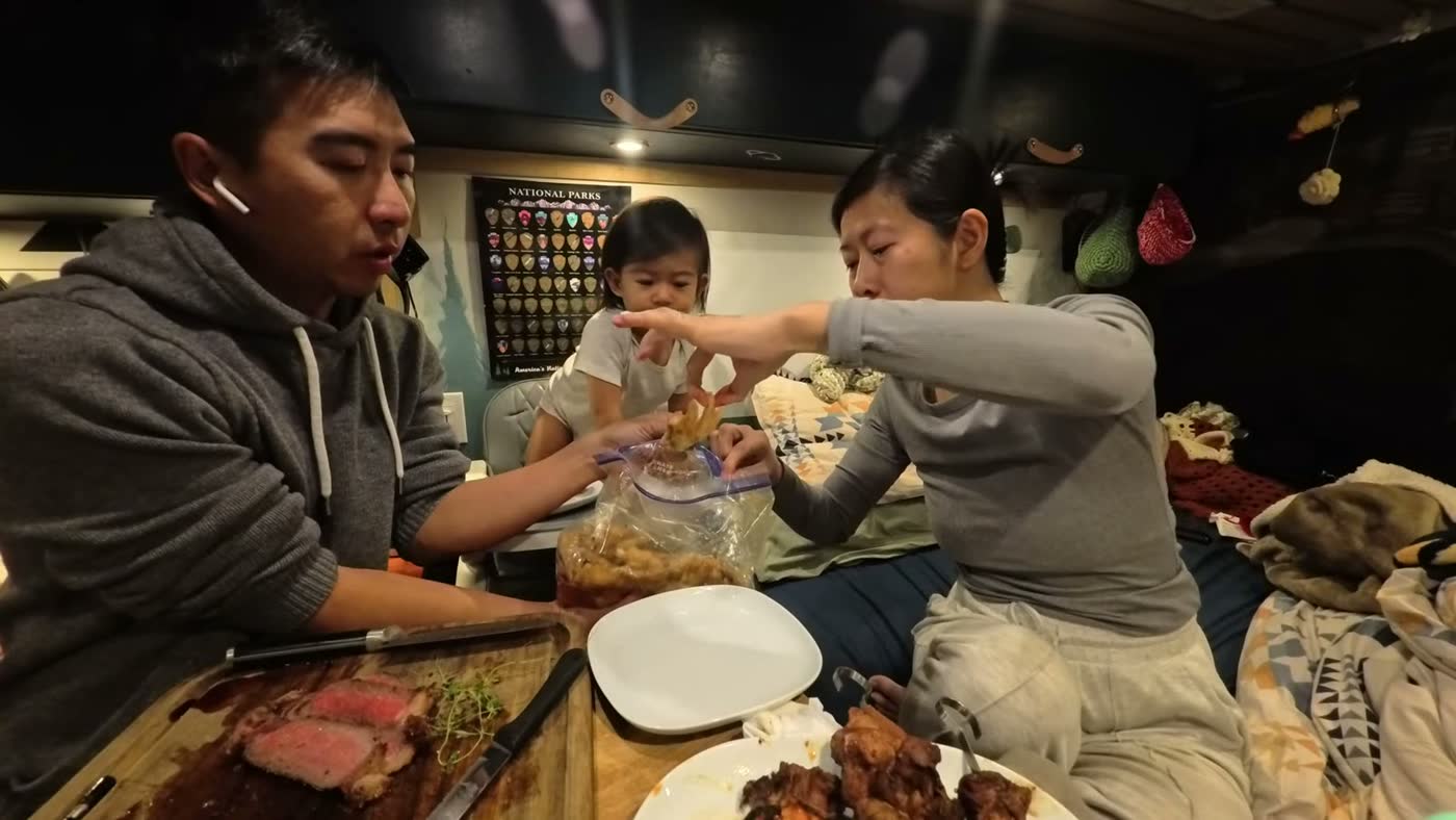 Rina taking a chicken foot out of the marinade bag at dinner in our van, with Spencer in his high chair