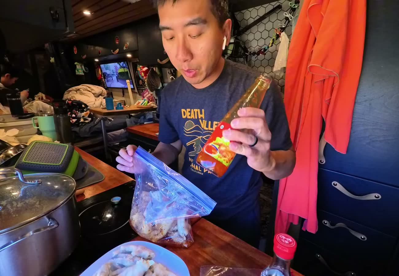 Michael holding a bottle of sweet chili sauce over a zip-top bag of chicken feet in the van kitchen