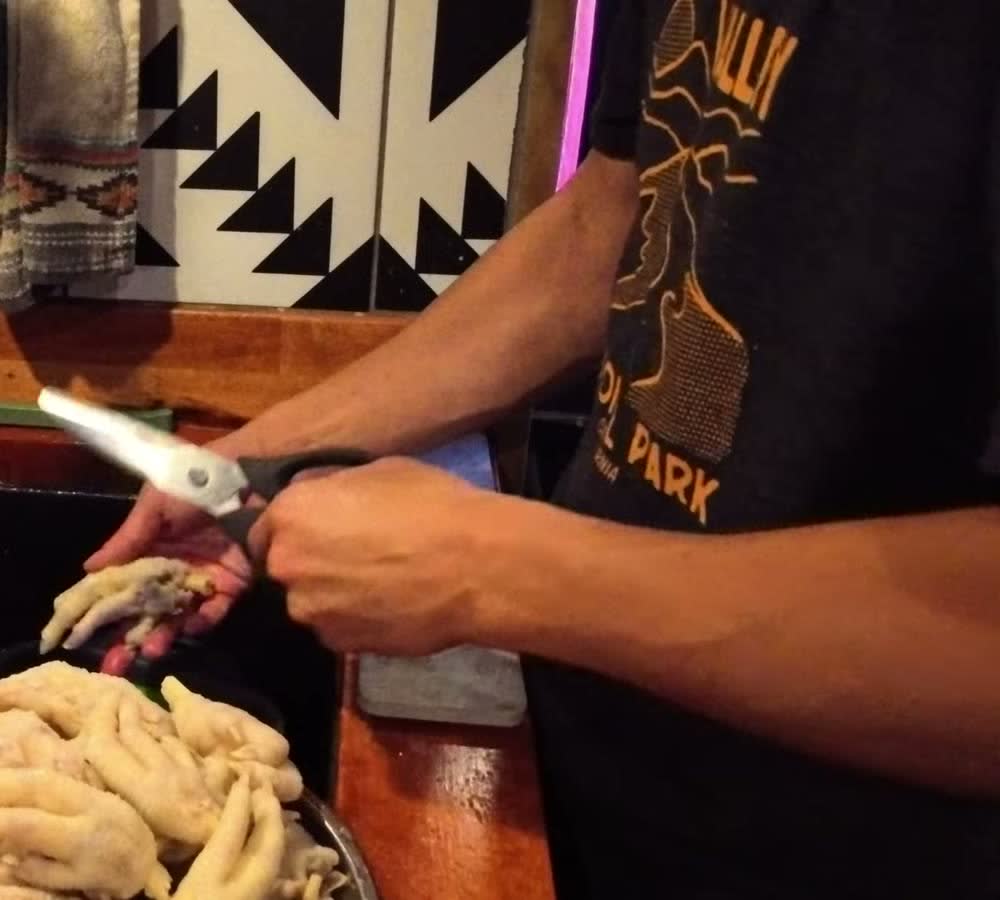 Michael trimming the nails off blanched chicken feet with kitchen scissors over the van sink