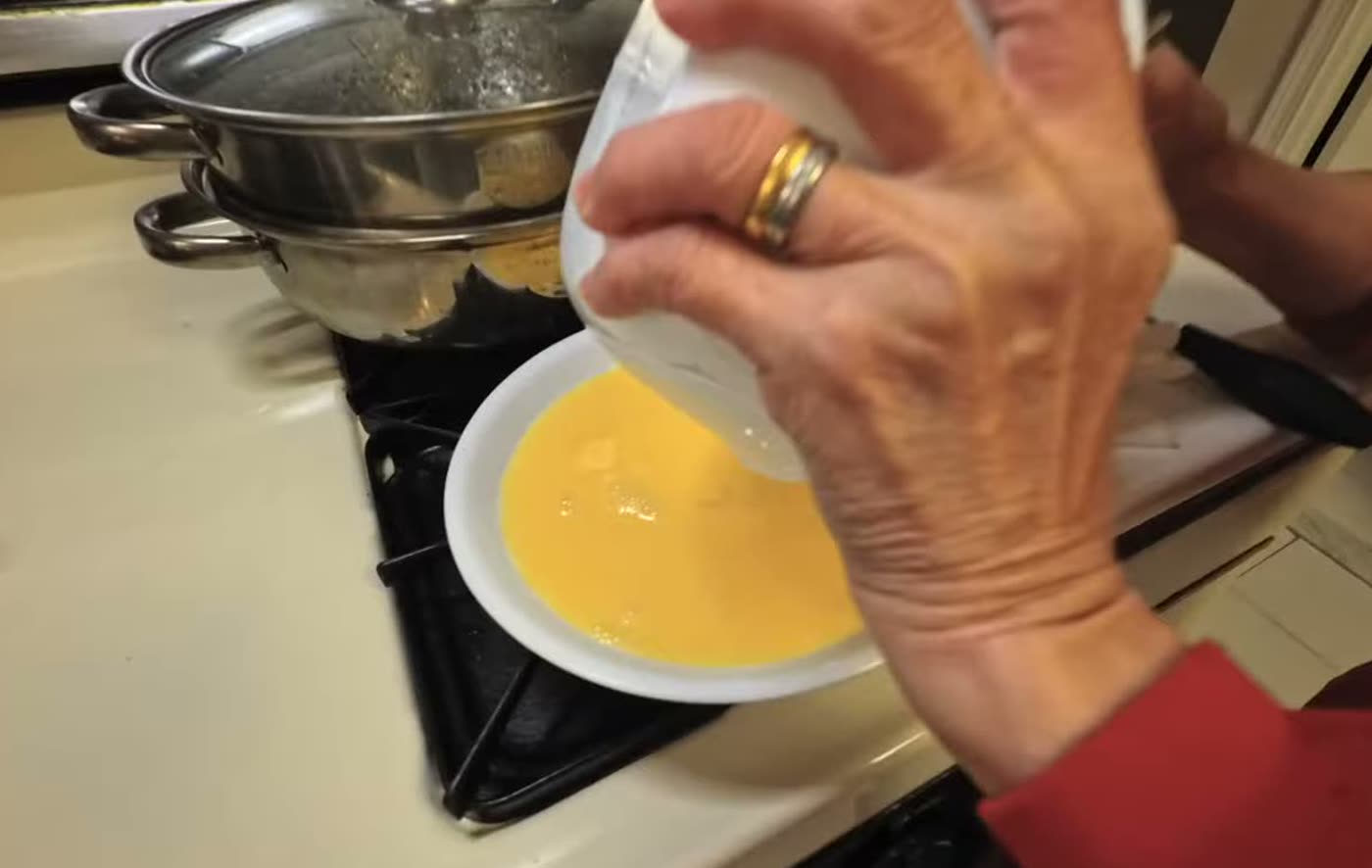 My mom pouring the beaten egg into a white plate next to the steamer