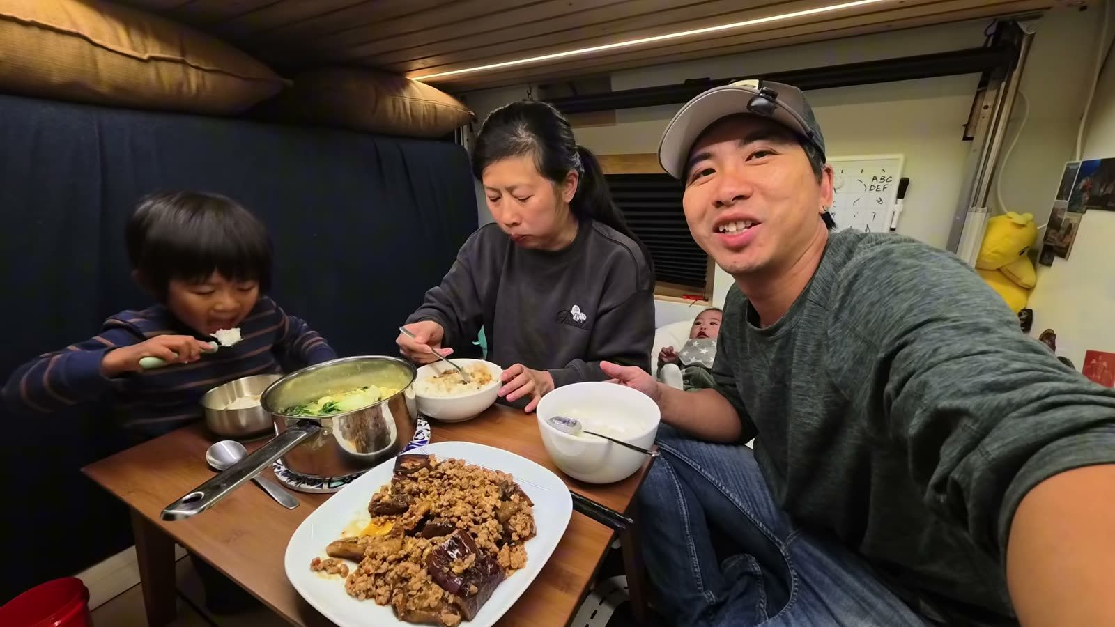 Spencer, Rina and Michael at the van table with the eggplant, the soup and bowls of rice