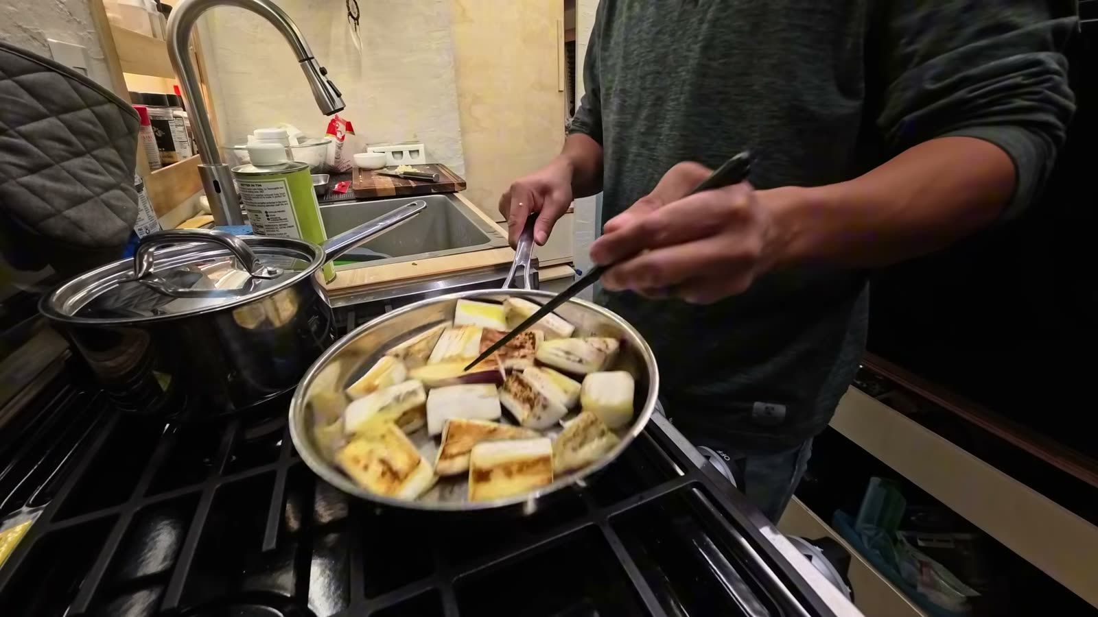 Pieces of eggplant frying in a stainless steel pan on the stove in our van
