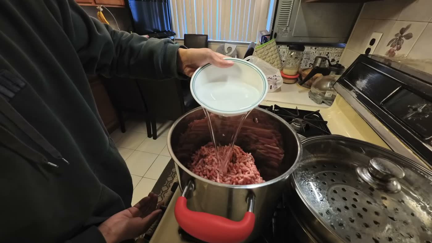 Michael pouring water into a big pot of ground beef fat trimmings on a kitchen stove