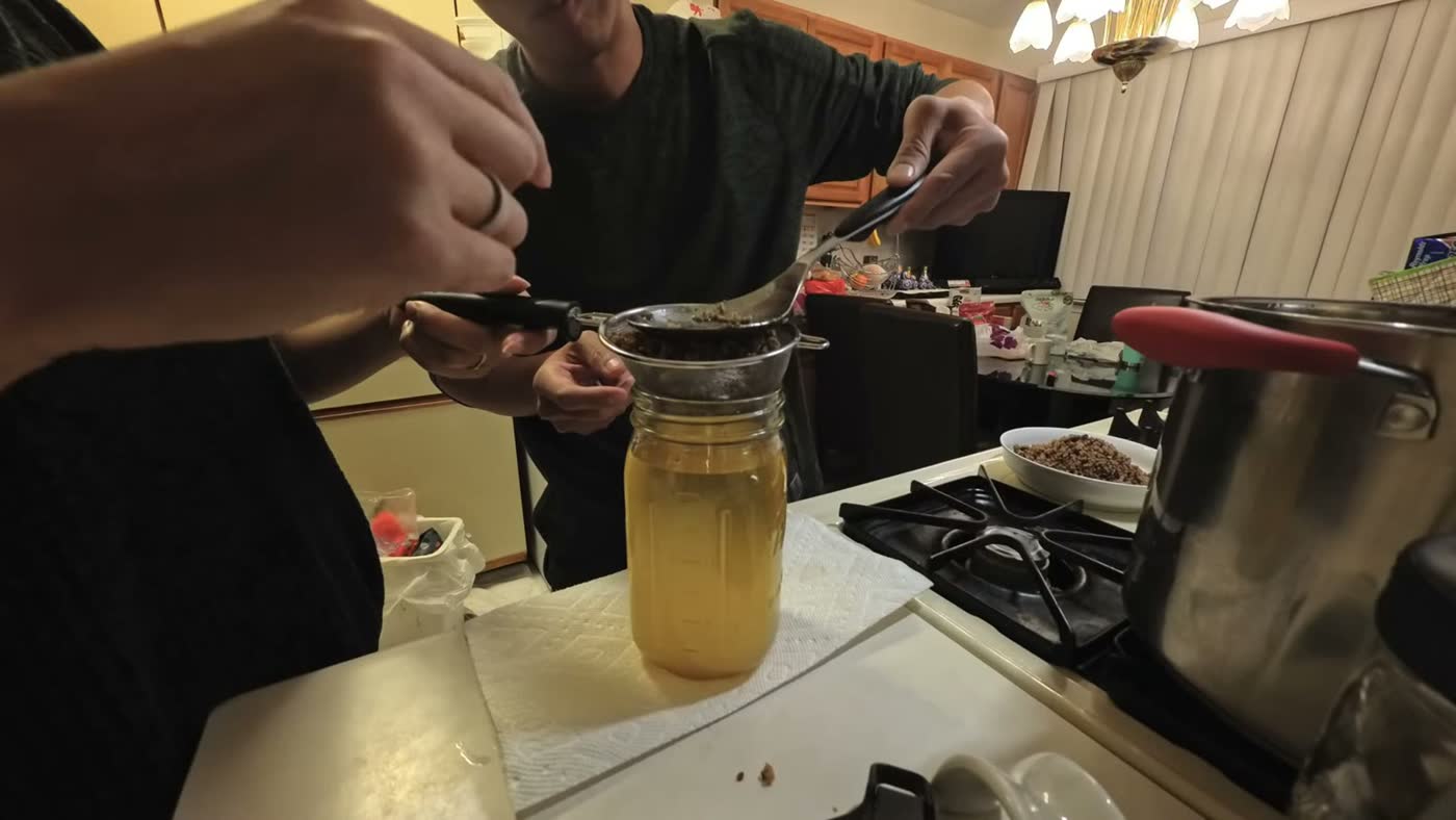 Michael straining homemade beef tallow through a mesh strainer into a mason jar