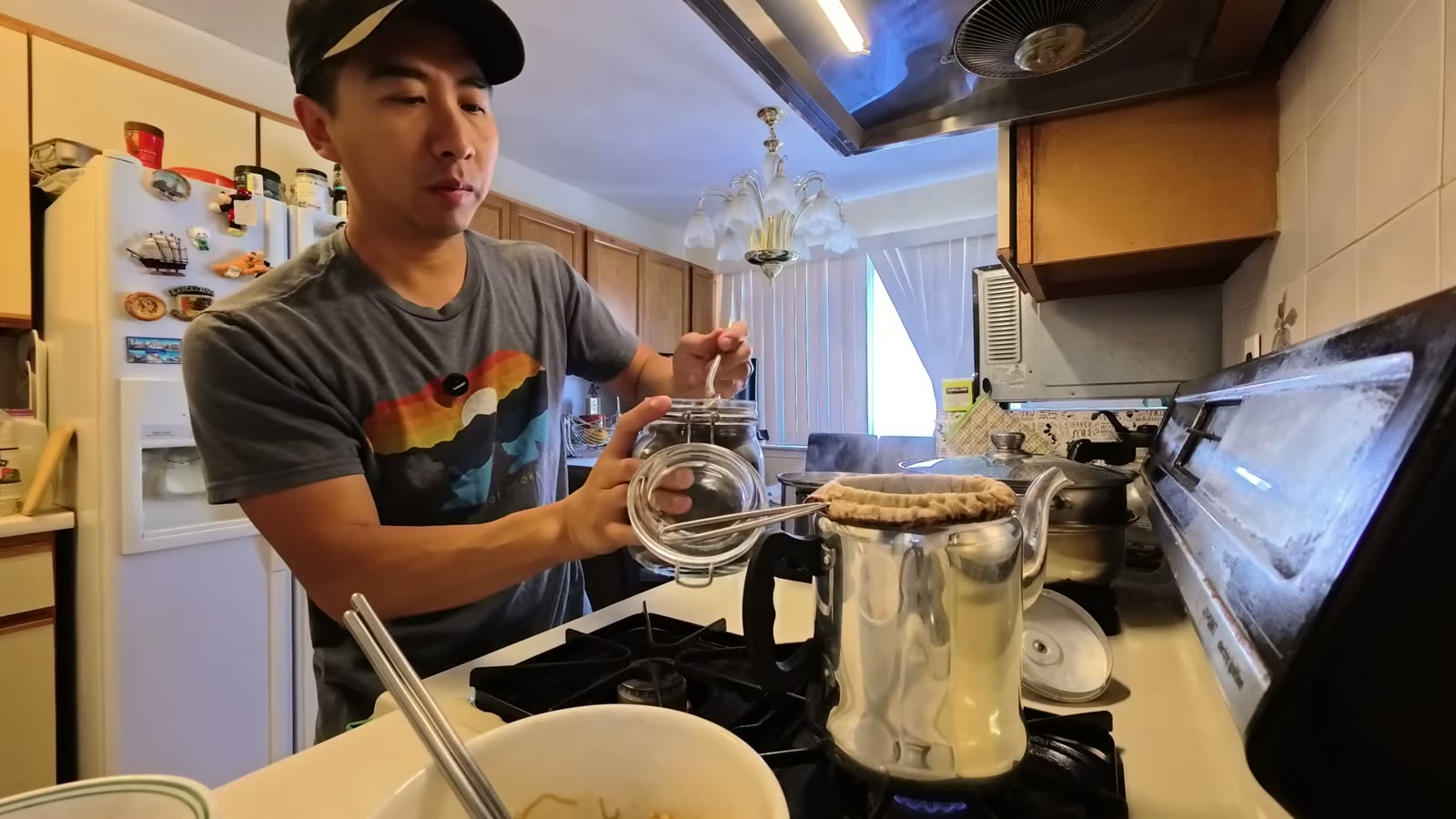 An aluminum milk tea pot with a cloth filter on the stove, with a jar of loose black tea next to it