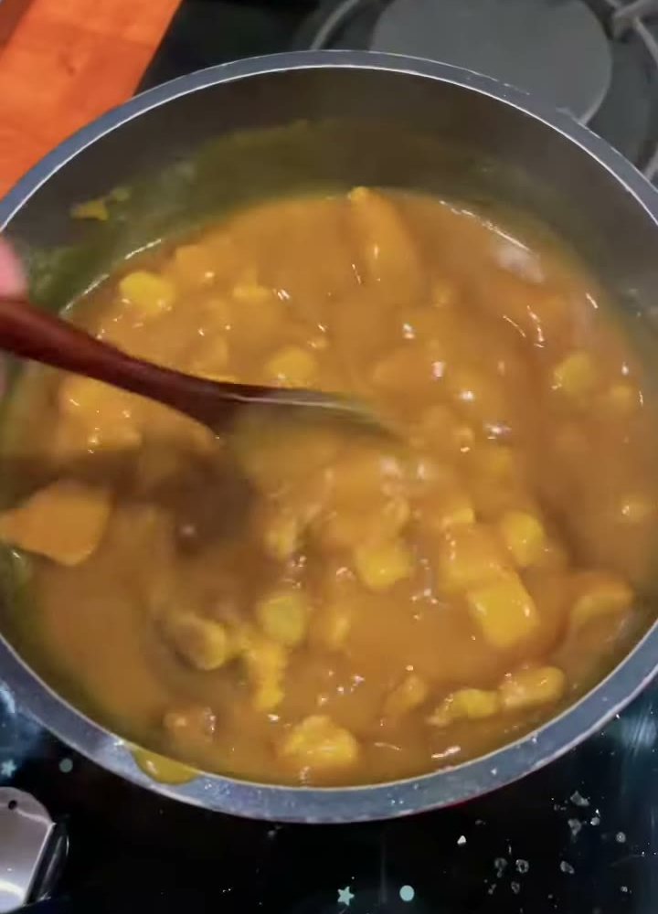 Japanese curry sauce simmering with chicken and potatoes, stirred with a wooden spoon