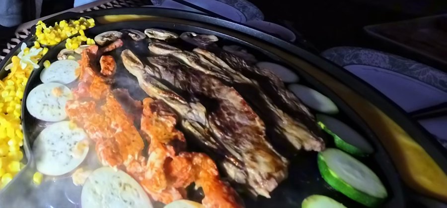 Short ribs and marinated pork and squid grilling in the middle of the pan, with corn, eggplant and zucchini around them