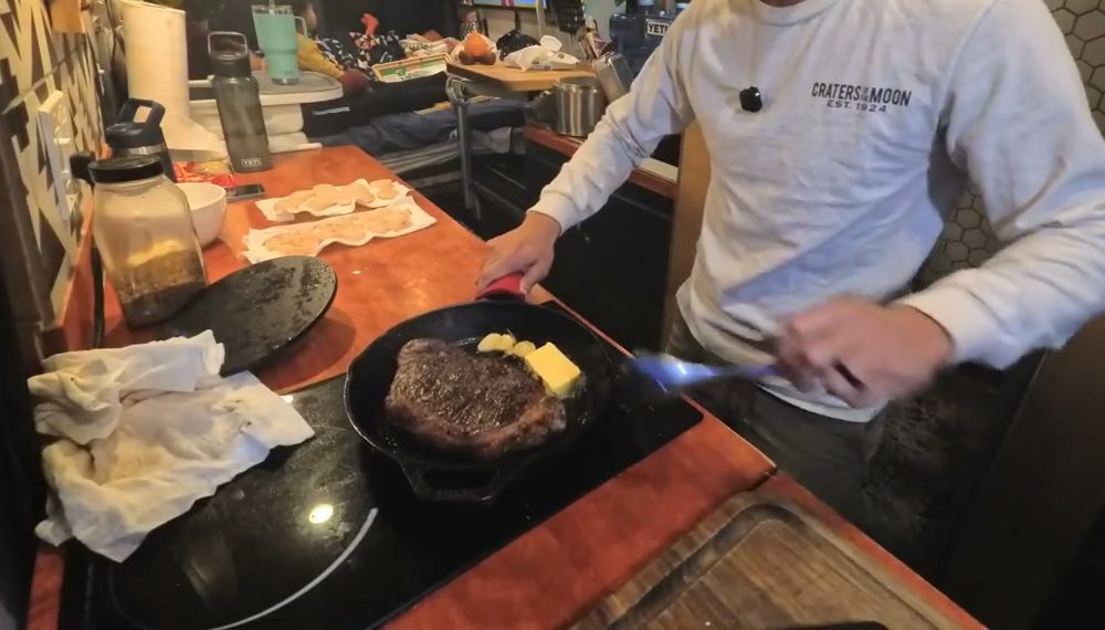 The steak searing in a cast iron pan with butter and garlic on an induction cooktop in our van
