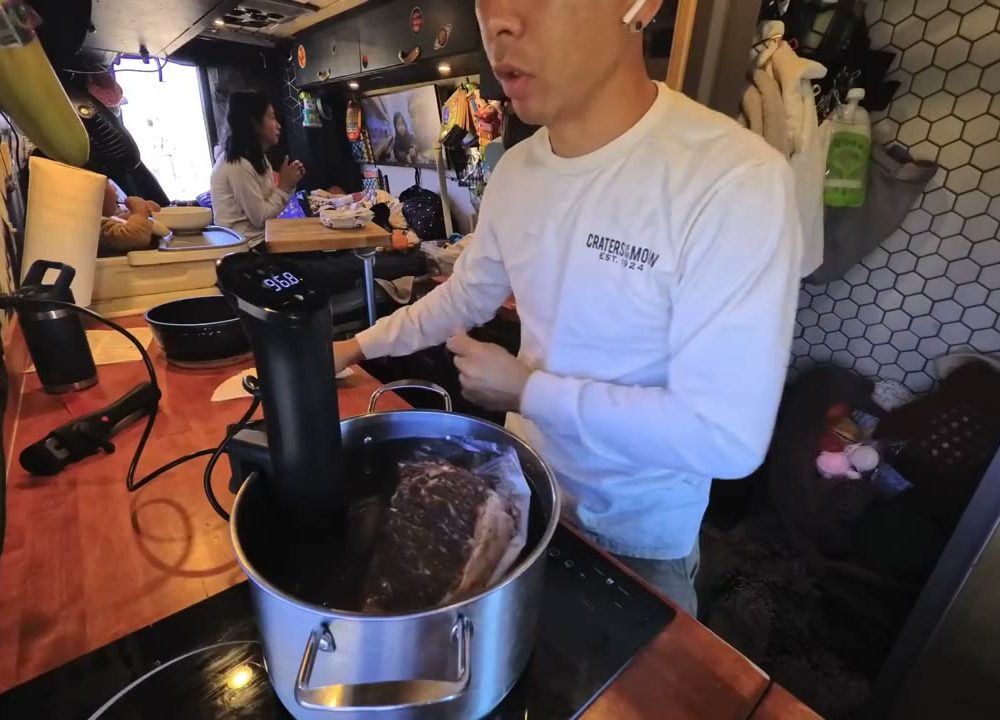 A steak in a vacuum-sealed bag in a pot of water with a sous vide cooker clipped on, on the van counter